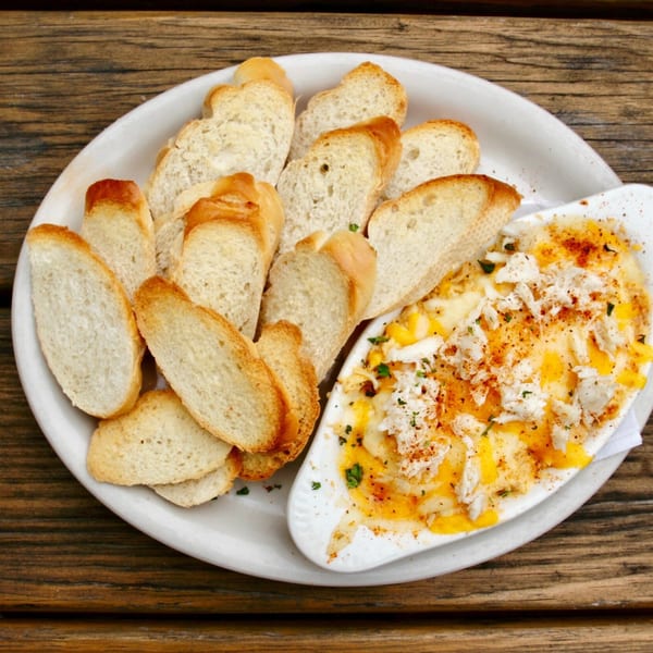 Stan & Joe's Saloon's crab dip with toasted baguette slices on a white plate.