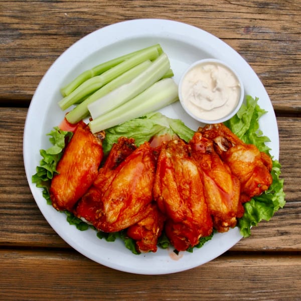 Stan & Joe's Saloon's buffalo wings with celery sticks and ranch dressing on a white plate.