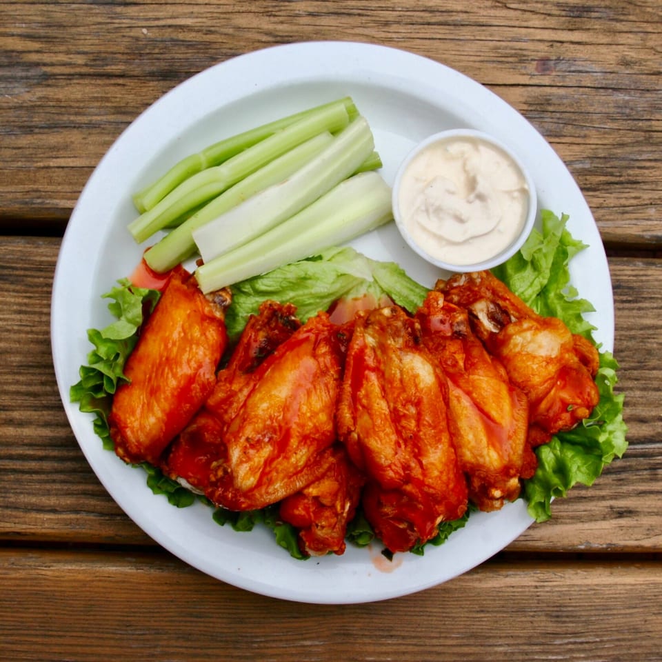 Stan & Joe's Saloon's buffalo wings with celery sticks and ranch dressing on a white plate.