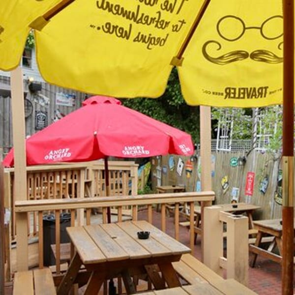 Outdoor patio at Stan & Joe's Saloon with wooden picnic tables, red and yellow umbrellas, and a decorated fence.