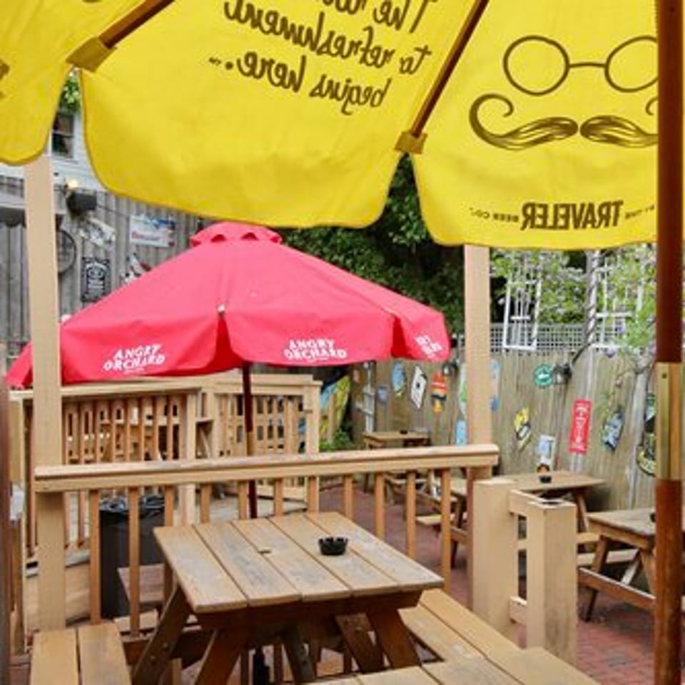 Outdoor patio at Stan & Joe's Saloon with wooden picnic tables, red and yellow umbrellas, and a decorated fence.