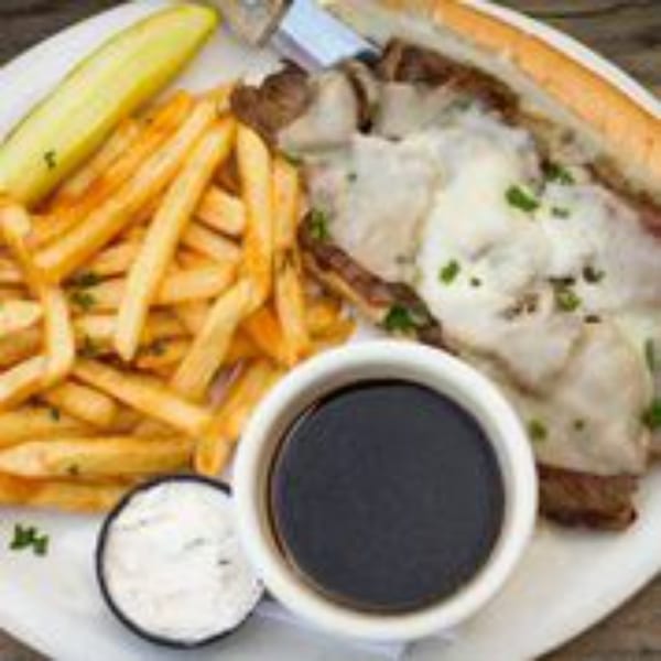 Stan & Joe's Saloon's French dip sandwich with fries, a pickle, and dipping sauces.
