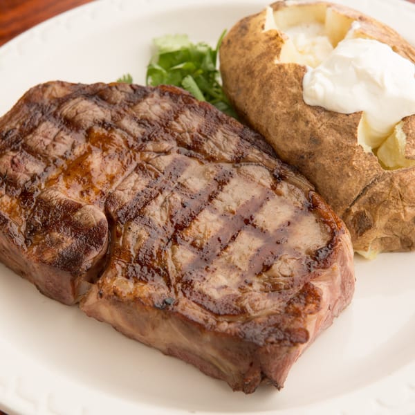 Grilled steak with grill marks, a baked potato topped with sour cream, and a sprig of parsley.