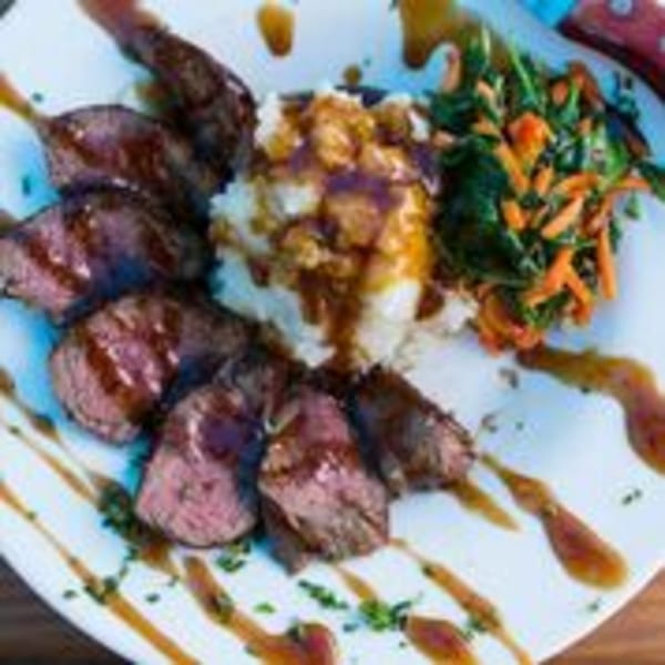 Plated bar-and-grill meal with sliced steak, mashed potatoes, and mixed greens with carrots.
