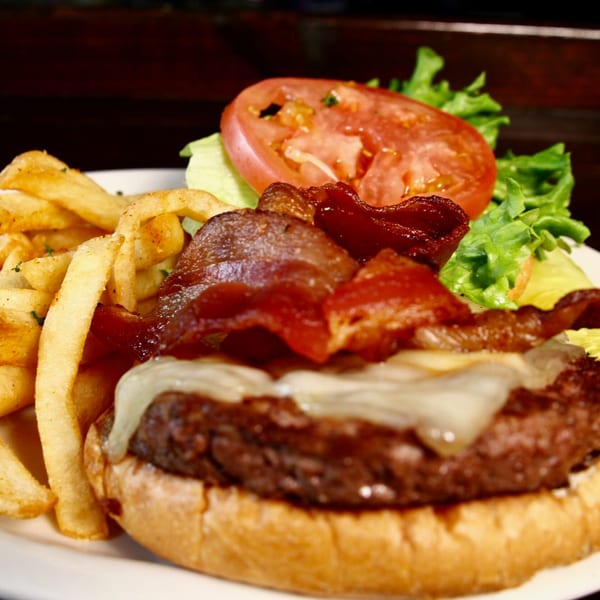 A Stan & Joe's Saloon bacon cheeseburger with fries, lettuce, and tomato on a white plate.