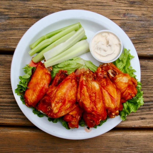 Stan & Joe's Saloon's buffalo wings, celery sticks, and dipping sauce on a white plate.