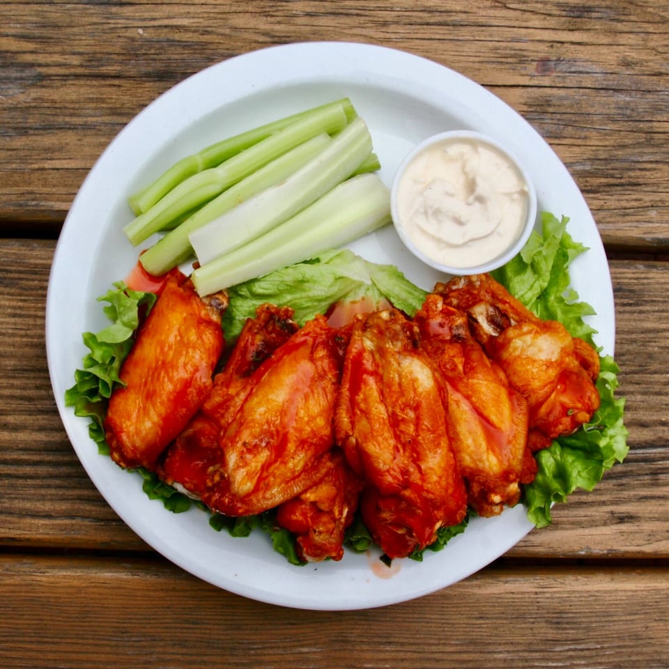 Stan & Joe's Saloon's buffalo wings, celery sticks, and dipping sauce on a white plate.