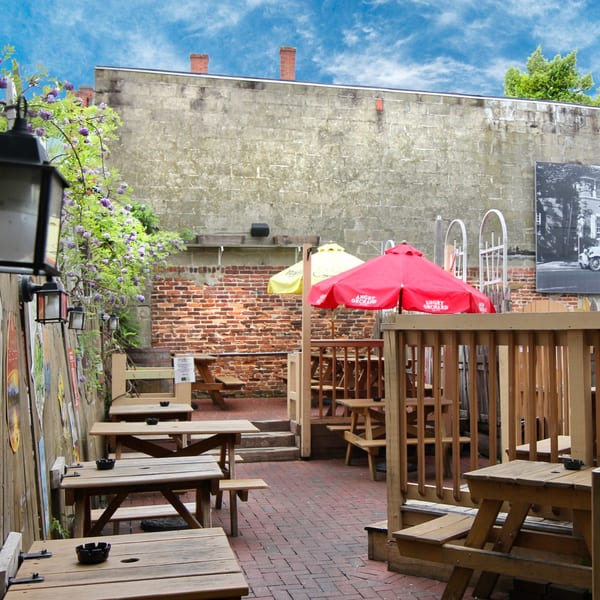 Stan & Joe's Saloon's outdoor patio with picnic tables, red and yellow umbrellas, and brick walls.