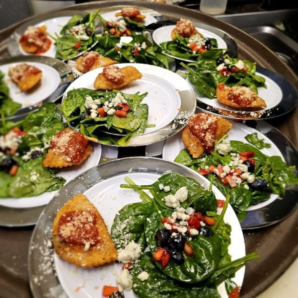 Multiple plates of spinach salad with berries, feta, and fried ravioli on a serving tray.