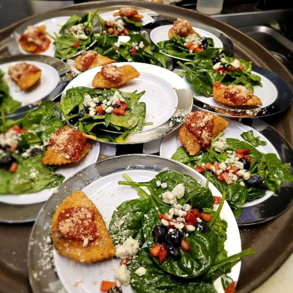 Multiple plates of spinach salad with berries, feta, and fried ravioli on a serving tray.