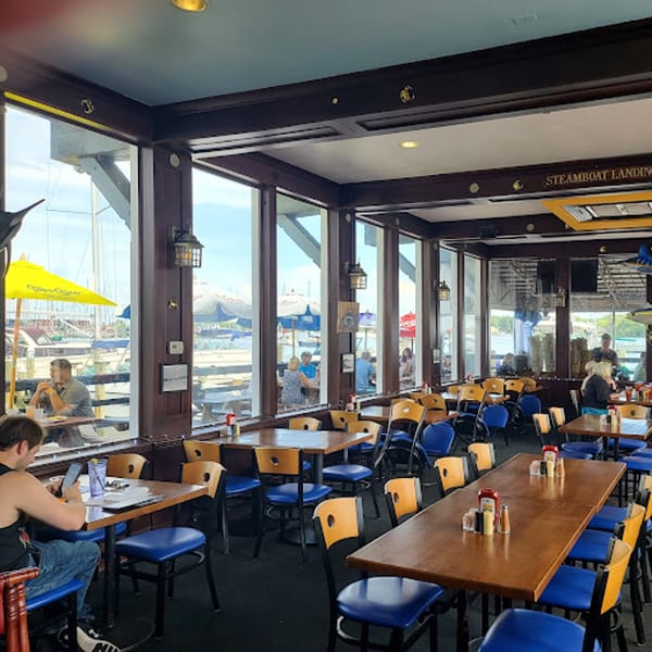 Stan & Joe's Saloon dining room with blue and yellow chairs, wooden tables, and large windows overlooking a marina.