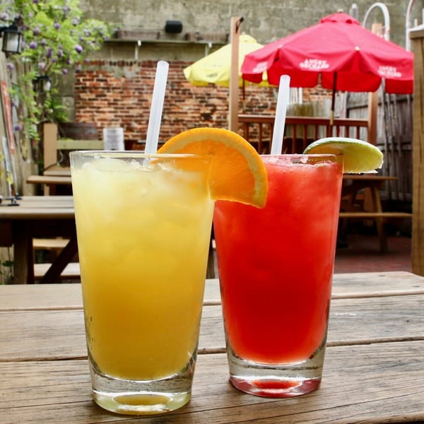 Two colorful cocktails, one orange and one red, on a wooden table at Stan & Joe's Saloon.