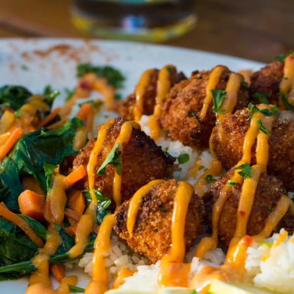 Crispy fried chicken or fish bites drizzled with orange sauce, served with rice and sautéed greens.