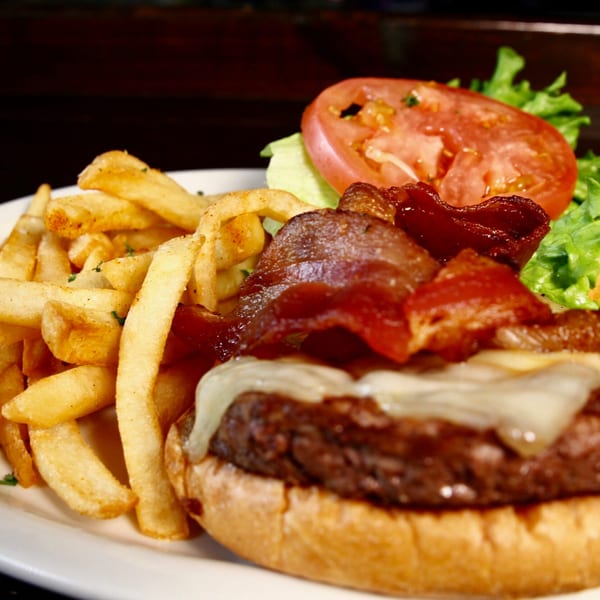 A Stan & Joe's Saloon bacon cheeseburger with fries, lettuce, and tomato on a white plate.