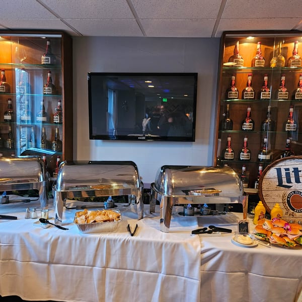 Buffet table with chafing dishes, chips, sliders, and condiments, flanked by liquor display cases.